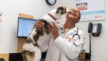 Banfield vet smiling and holding a dog in exam room